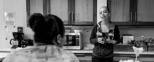 Una mujer bebe café mientras conversa con otra mujer, en la cocina.