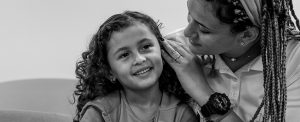 Una madre sostiene el pelo de su hija mientras le susurra al oído. La niña sonríe.