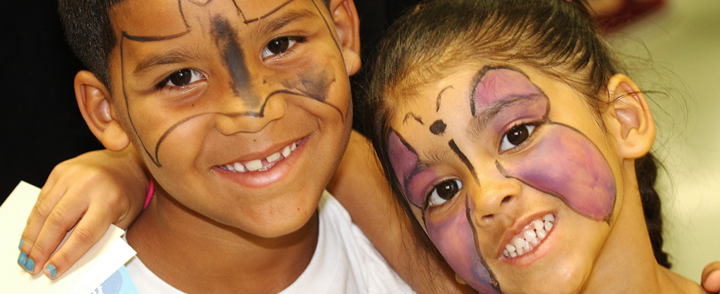 Niño y niña sonrientes con sus caras pintadas con motivos de mariposa y Batman. La niña sostiene un papel en su mano derecha.